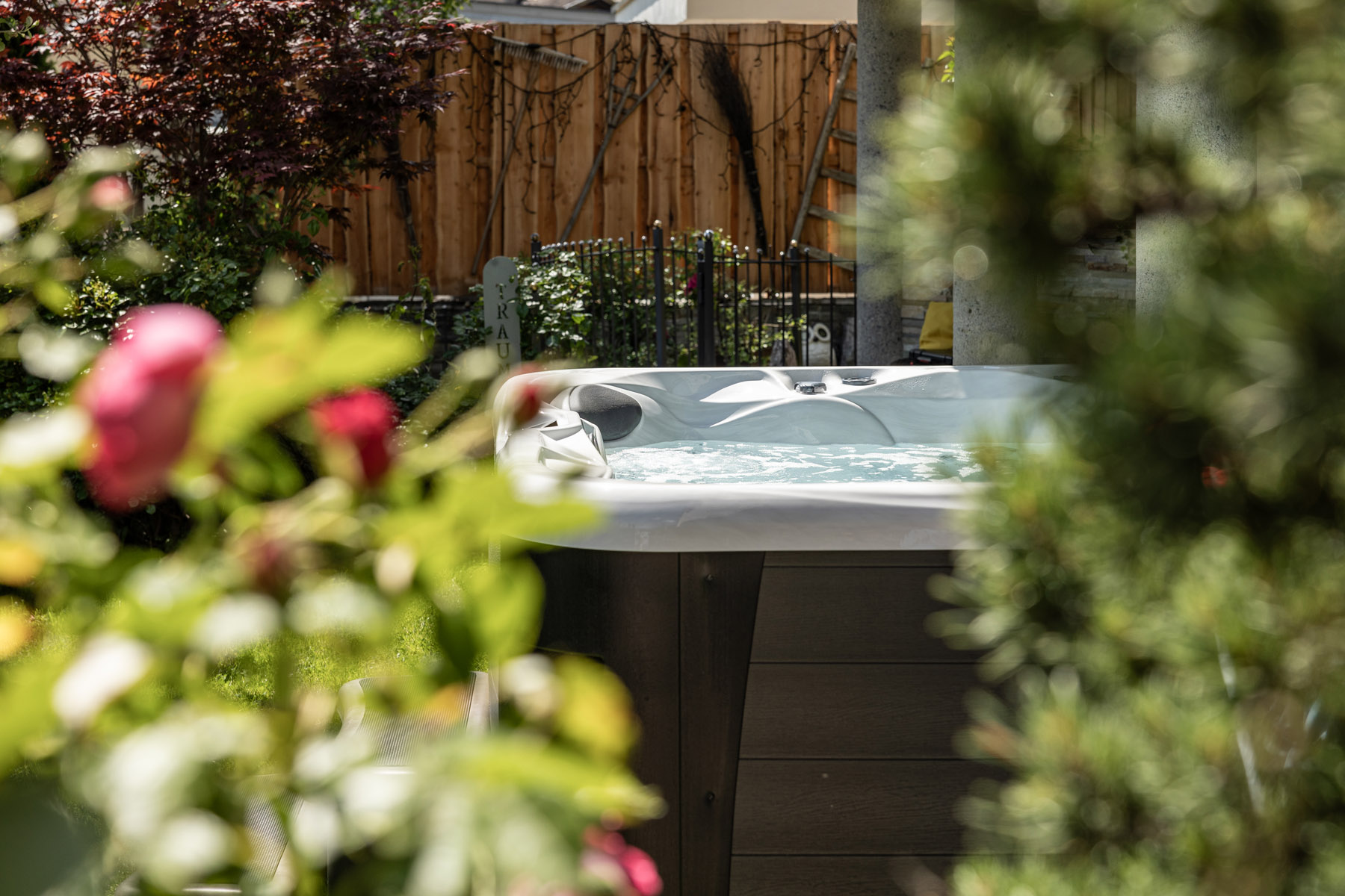 Ein Whirlpool in einem Garten, teilweise verdeckt durch Pflanzen und Blumen im Vordergrund.