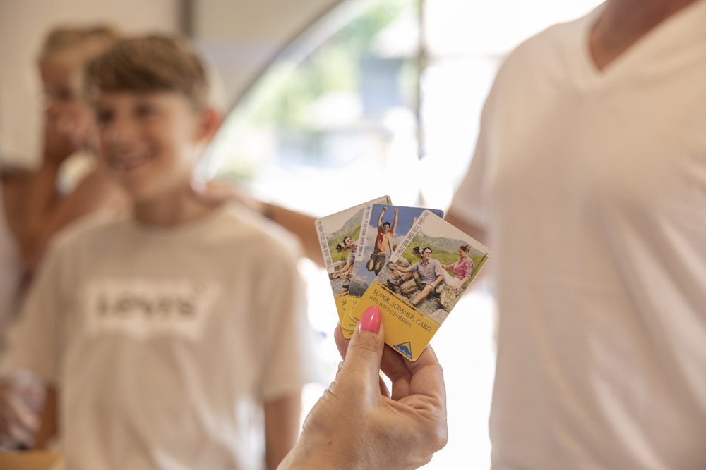 Drei Touristenkarten in der Hand; Familie checkt für Sommerurlaub in Serfaus-Fiss-Ladis ein.