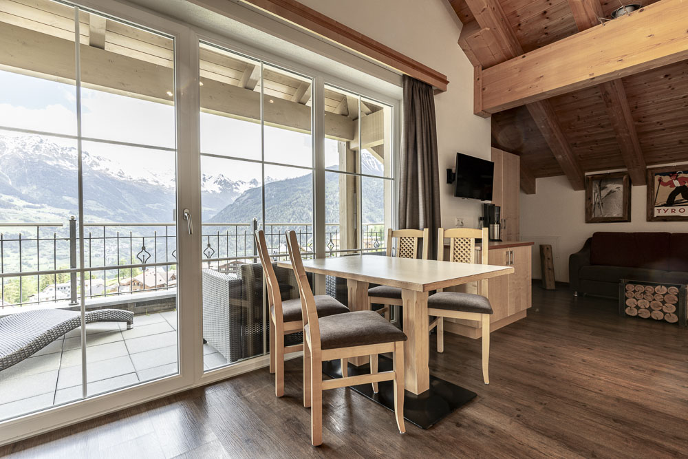 Heller alpiner Essbereich mit Holztisch, Bergblick und Balkon durch Glastüren.