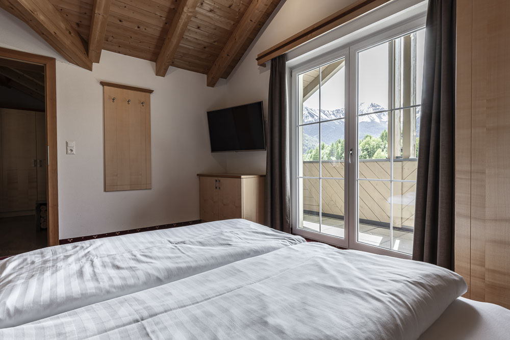 Gemütliches Schlafzimmer mit Doppelbett, schräger Holzdecke und Bergblick durch Glastüren.