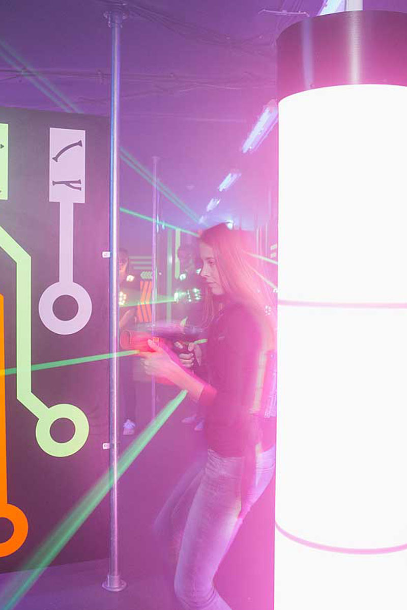Frau spielt Laser-Tag, hält einen Blaster, umgeben von Neonlicht und Nebel.