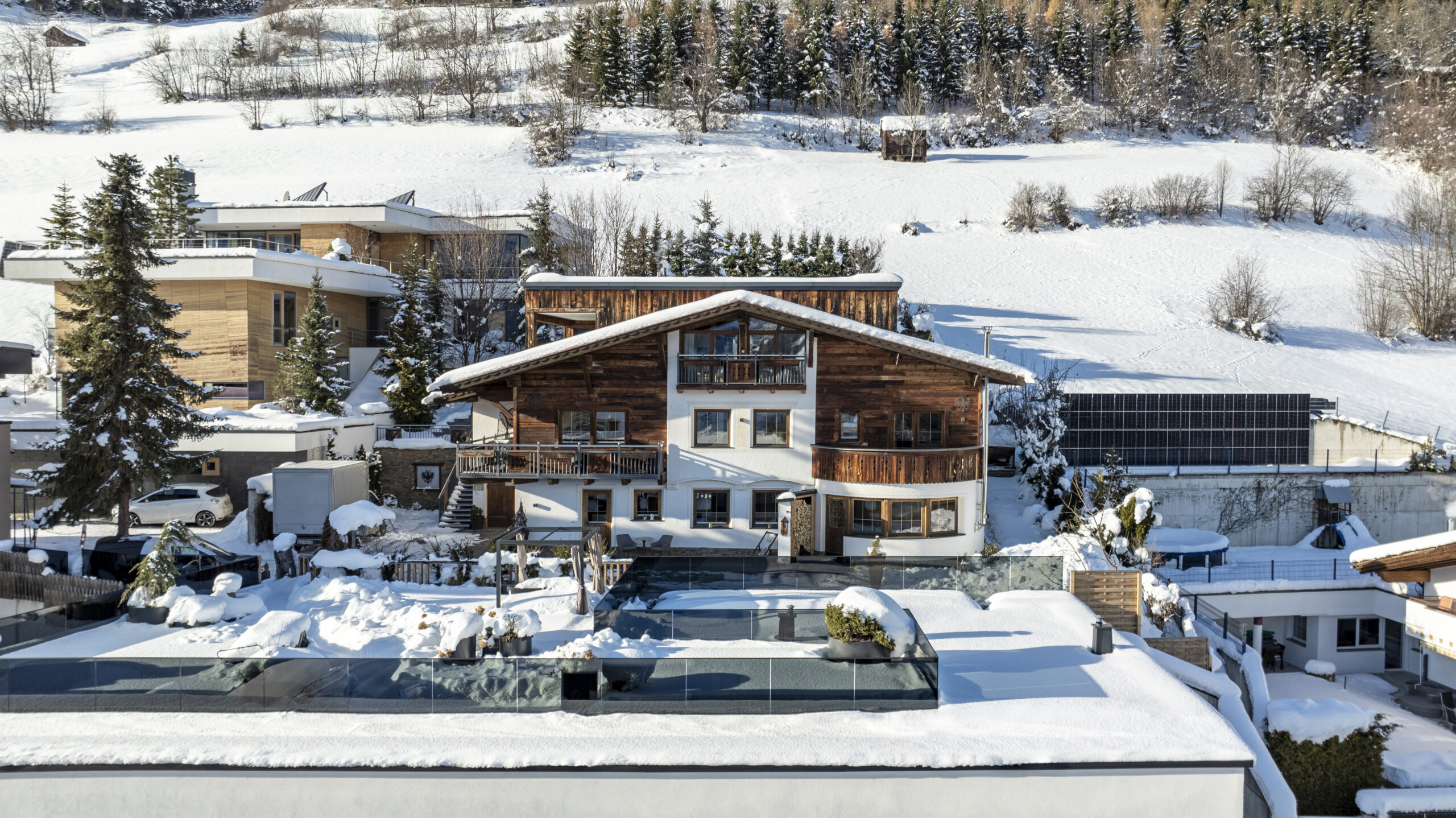 Ein großes Holzchalet, die Naturlodge am Waldesrand in Ladis, inmitten von Schnee und Kiefern.