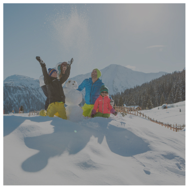 Vier Menschen in Winterkleidung genießen den Schnee neben einem Schneemann bei Alpenresorts, im Hintergrund die Berge.